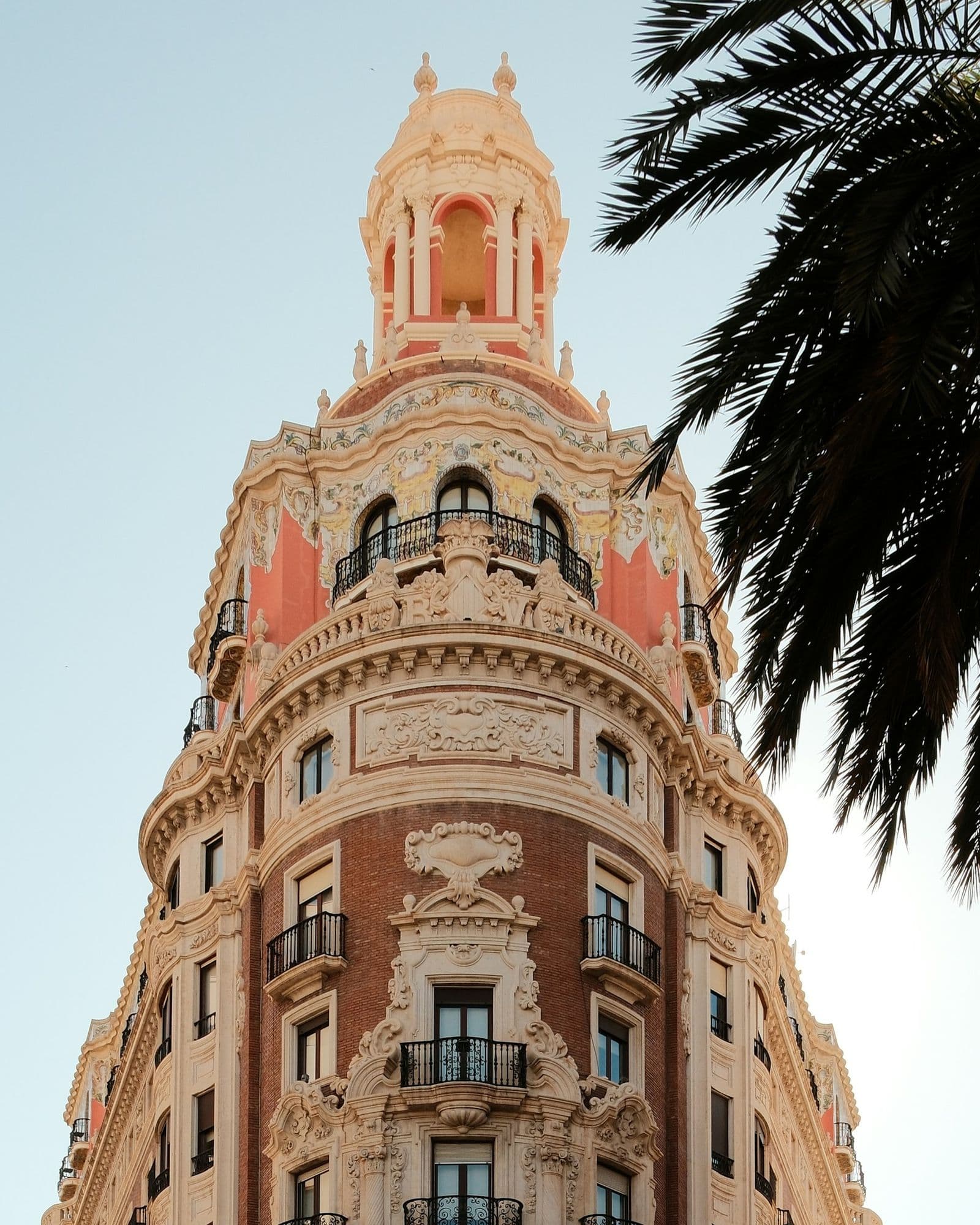 Torre del edificio del Banco de Valencia junto a una palmera, con la luz baja de la tarde
